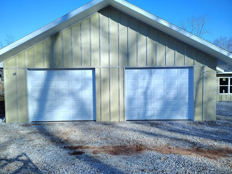 Elite Garage Door Services of Northwest ArkansasA beige building with two closed white residential garage doors under a clear blue sky, representing reliable garage door service in Northwest Arkansas. Gravel driveway leads to the garage, emphasizing a local touch in Rogers AR.