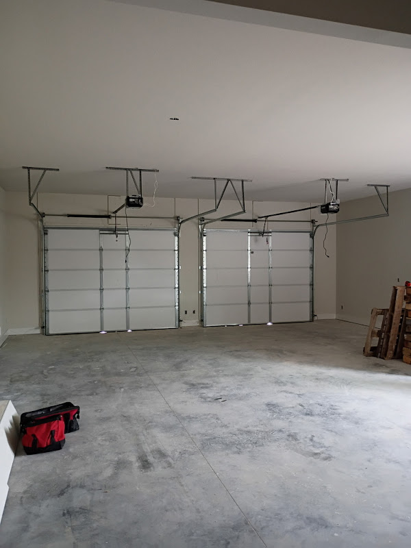 Elite Garage Door Services of Northwest ArkansasA spacious garage in Northwest Arkansas with three closed overhead garage doors and visible garage door openers, highlighting professional garage door installation services. A red tool bag is on the floor, suggesting ongoing work or maintenance.