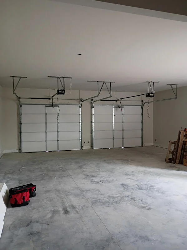 Elite Garage Door Services of Northwest ArkansasA spacious garage in Northwest Arkansas with three closed overhead garage doors and visible garage door openers, highlighting professional garage door installation services. A red tool bag is on the floor, suggesting ongoing work or maintenance.