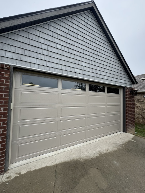 Elite Garage Door Services of Northwest ArkansasA beige residential garage door with windows in a brick house, showcasing a recent garage door installation in Northwest Arkansas, emphasizing local and professional service.