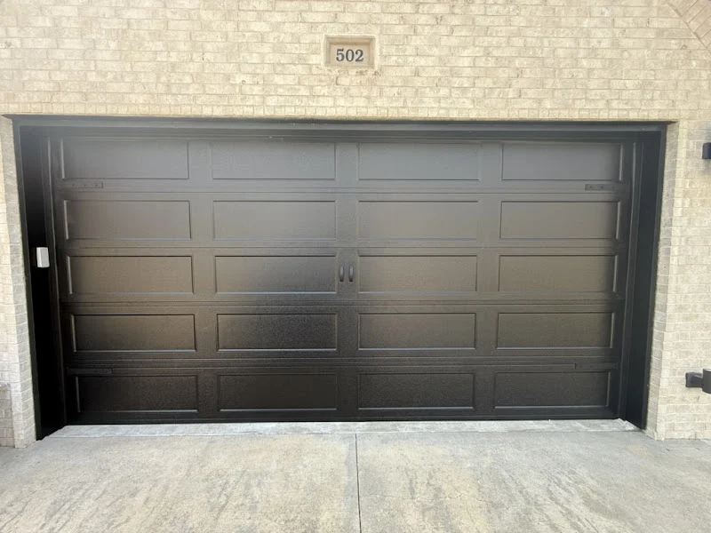 Elite Garage Door Services of Northwest ArkansasA sleek black residential garage door is closed against a light brick wall, showcasing a professional garage door installation in Northwest Arkansas.