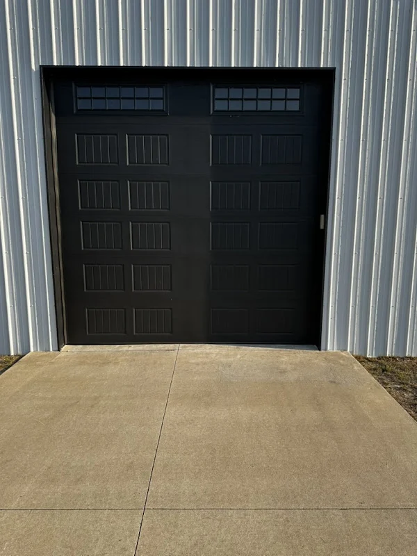 Elite Garage Door Services of Northwest ArkansasA black residential garage door with windowed panels is installed on a metal building in Northwest Arkansas, reflecting Elite Garage Door's professional and reliable service in Rogers AR and surrounding areas.