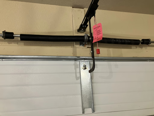 Elite Garage Door Services of Northwest ArkansasA close-up image of a residential garage door spring system being repaired by a professional in Northwest Arkansas. The black overhead spring is mounted above a white door, showcasing the intricate parts involved in garage door repair.