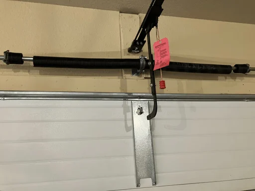 Elite Garage Door Services of Northwest ArkansasA close-up image of a residential garage door spring system being repaired by a professional in Northwest Arkansas. The black overhead spring is mounted above a white door, showcasing the intricate parts involved in garage door repair.