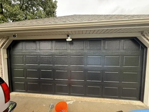Elite Garage Door Services of Northwest ArkansasA newly installed black residential garage door is seen in a suburban setting. The scene suggests a recent garage door installation in Northwest Arkansas, highlighting professional and reliable local garage door service.