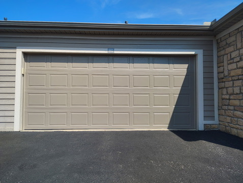 Elite Garage Door Services of Northwest ArkansasA tan residential garage door is closed, casting a shadow on the black asphalt driveway. The image depicts a typical home in Northwest Arkansas, highlighting the reliability of local garage door service providers.