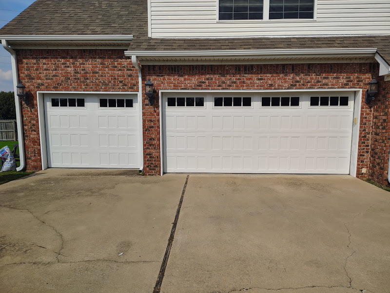 Elite Garage Door Services of Northwest ArkansasA brick house with two white residential garage doors featuring small windows at the top, located in Northwest Arkansas. The driveway is clean and well-maintained, showcasing the results of a professional garage door installation service.