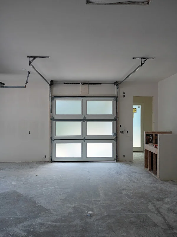 Elite Garage Door Services of Northwest ArkansasA newly installed frosted glass overhead garage door in a clean, unfinished garage space in Northwest Arkansas, showcasing modern residential garage doors with a focus…