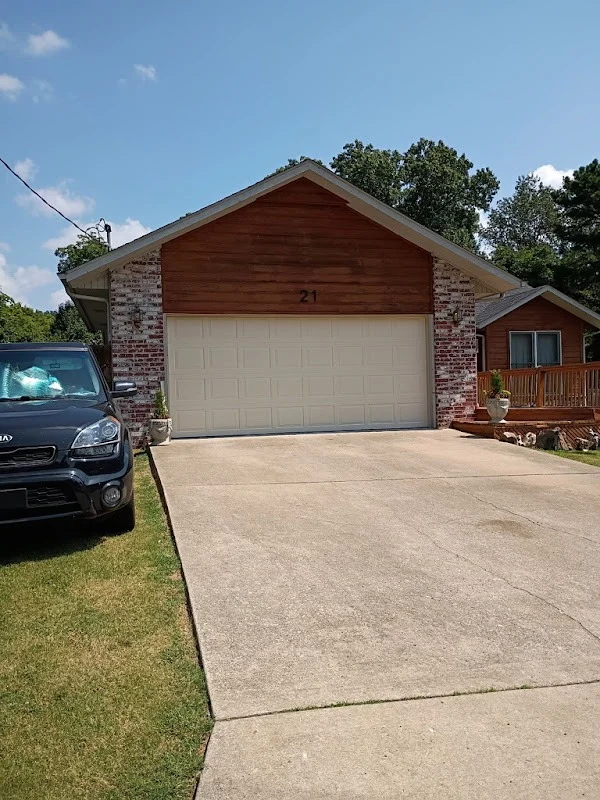 Elite Garage Door Services of Northwest ArkansasA residential home in Northwest Arkansas with a closed, white overhead garage door and a black car parked on the lawn, under a clear blue sky. The scene highlights the need for reliable garage door service in the area.
