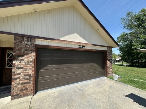Elite Garage Door Services of Northwest ArkansasA brown residential garage door is shown on a brick house in Northwest Arkansas under a clear blue sky, highlighting the need for reliable garage door service.