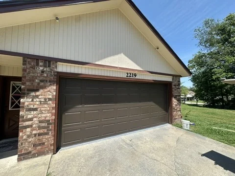 Elite Garage Door Services of Northwest ArkansasA brown residential garage door is shown on a brick house in Northwest Arkansas under a clear blue sky, highlighting the need for reliable garage door service.