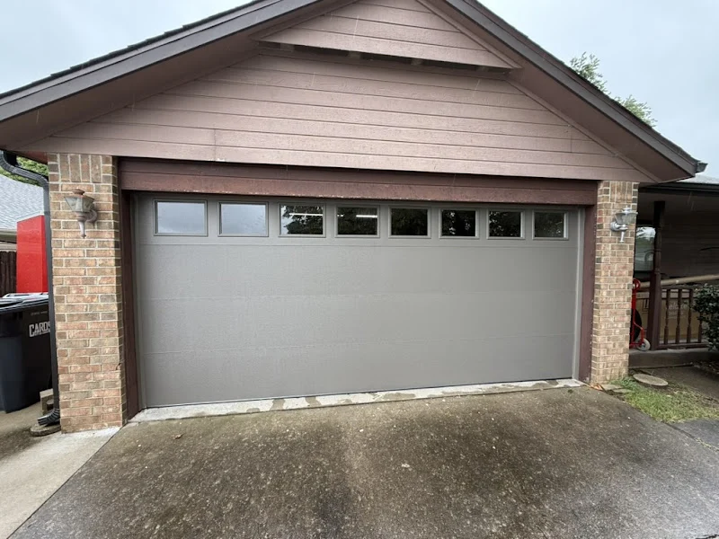 Elite Garage Door Services of Northwest ArkansasA newly installed residential garage door with small windows at the top in a brick-walled garage, showcasing professional garage door service in Northwest Arkansas.