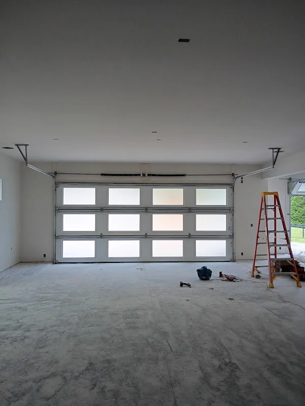Elite Garage Door Services of Northwest ArkansasA professional garage door installation is underway in a spacious, empty garage with overhead garage doors. Tools and a red ladder are visible, indicating ongoing…