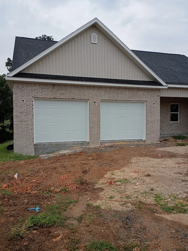 Elite Garage Door Services of Northwest ArkansasA newly constructed house in Northwest Arkansas features two white overhead garage doors, highlighting recent garage door installation for residential use in a local setting.