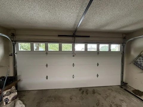 Elite Garage Door Services of Northwest ArkansasA white residential garage door with windows is closed inside a garage. The image highlights the potential need for garage door repair or installation services…