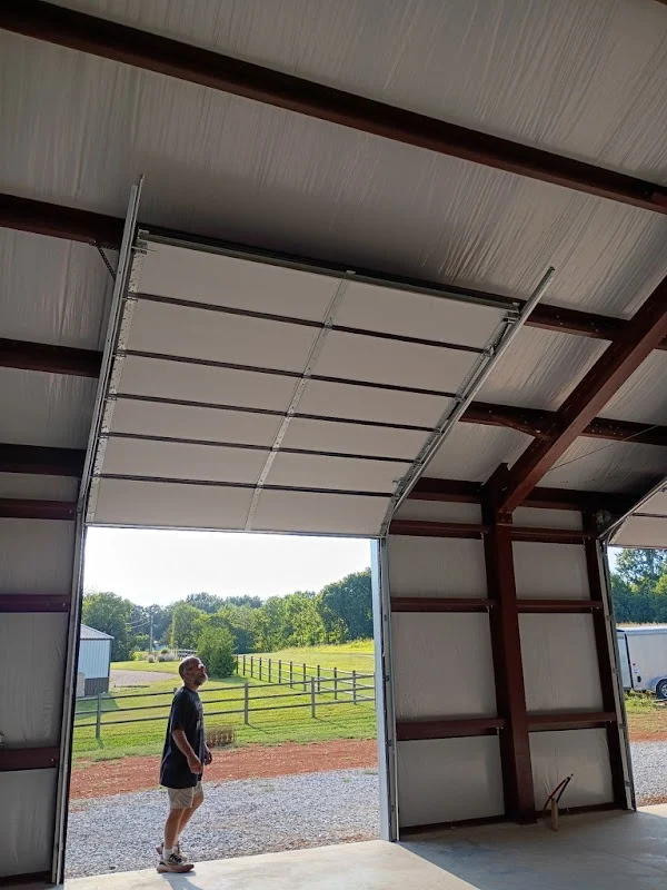 Elite Garage Door Services of Northwest ArkansasA professional technician inspects an overhead garage door installation in a spacious warehouse setting with a scenic view outside, highlighting reliable garage door service in Northwest Arkansas.