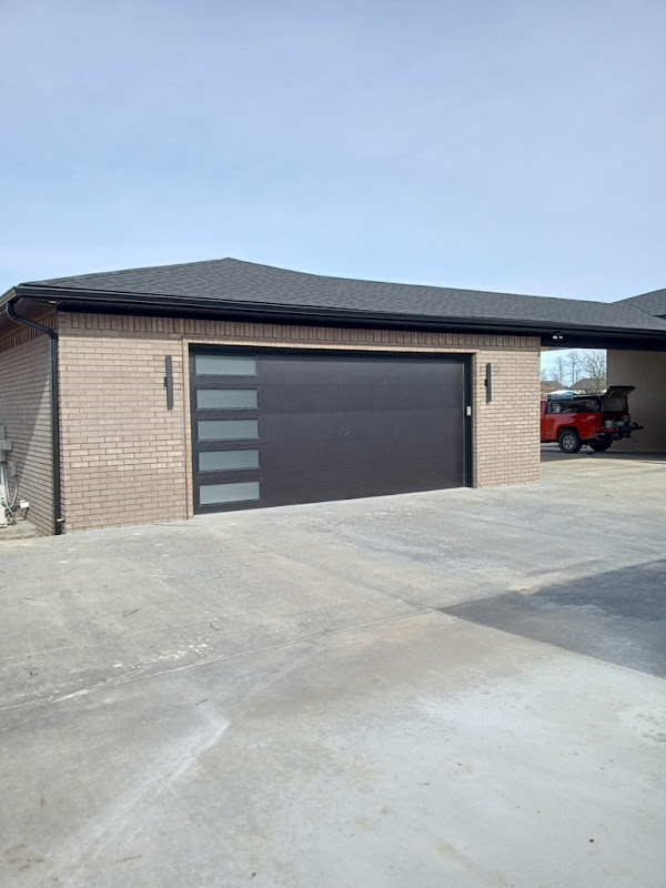 Elite Garage Door Services of Northwest ArkansasA modern residential garage with a sleek, dark overhead door and frosted glass panels, located in Northwest Arkansas, with a red vehicle parked nearby, showcasing a professional and reliable garage door installation.