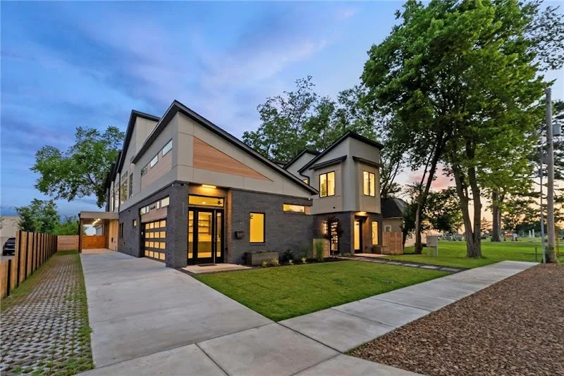 Elite Garage Door Services of Northwest ArkansasModern two-story home with a sleek design featuring overhead garage doors in Northwest Arkansas, surrounded by lush greenery and a well-maintained driveway under a twilight sky.