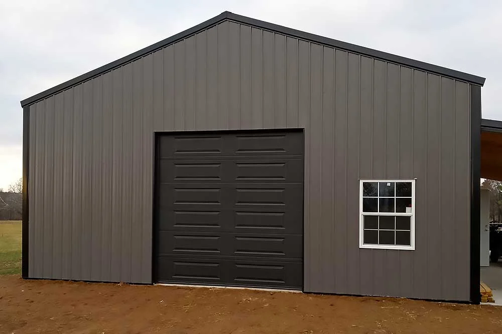 Farmington-image Elite Garage Door Services of Northwest Arkansas-A sleek gray metal building with a closed black overhead garage door and a window on the side, exemplifying modern residential garage doors. This structure highlights garage door installation services available in Northwest Arkansas.
