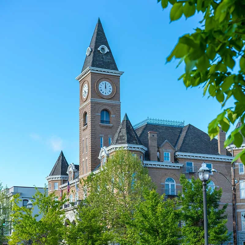 Elite Garage Door Services of Northwest Arkansas-Historic brick clock tower in Fayetteville AR, surrounded by lush green trees and blue sky, symbolizing the local charm of Northwest Arkansas, where reliable garage door service is available for residential garage doors and installations.