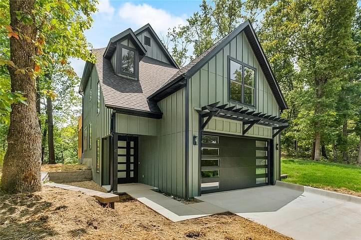 Elite Garage Door Services of Northwest ArkansasA modern green house with large windows and an attached garage featuring sleek, black overhead garage doors, surrounded by trees, showcasing residential garage doors in a serene Northwest Arkansas setting.