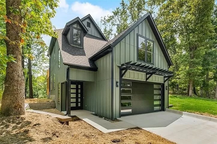 Elite Garage Door Services of Northwest ArkansasA modern green house with large windows and an attached garage featuring sleek, black overhead garage doors, surrounded by trees, showcasing residential garage doors in a serene Northwest Arkansas setting.