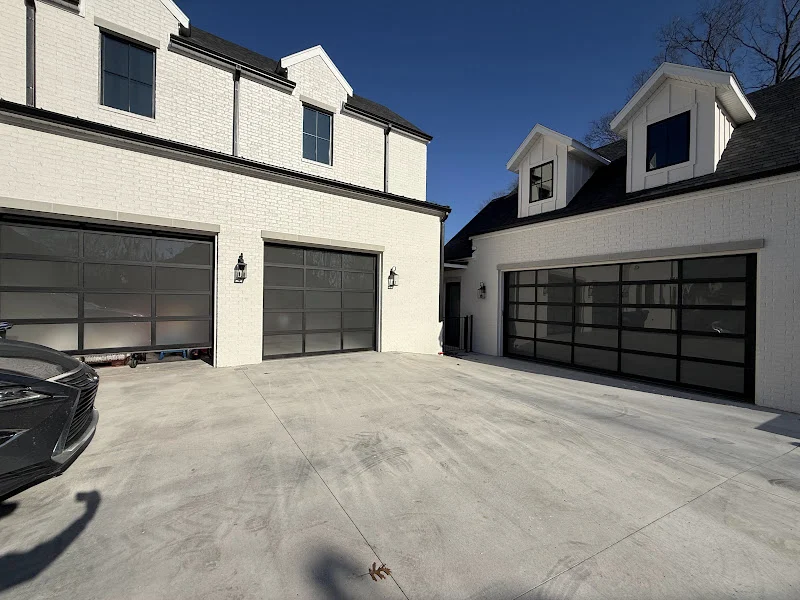 Elite Garage Door Services of Northwest ArkansasA modern home in Northwest Arkansas with sleek, black-framed residential garage doors under a clear blue sky. The driveway is spacious, highlighting the garage door installation's professional and reliable finish.