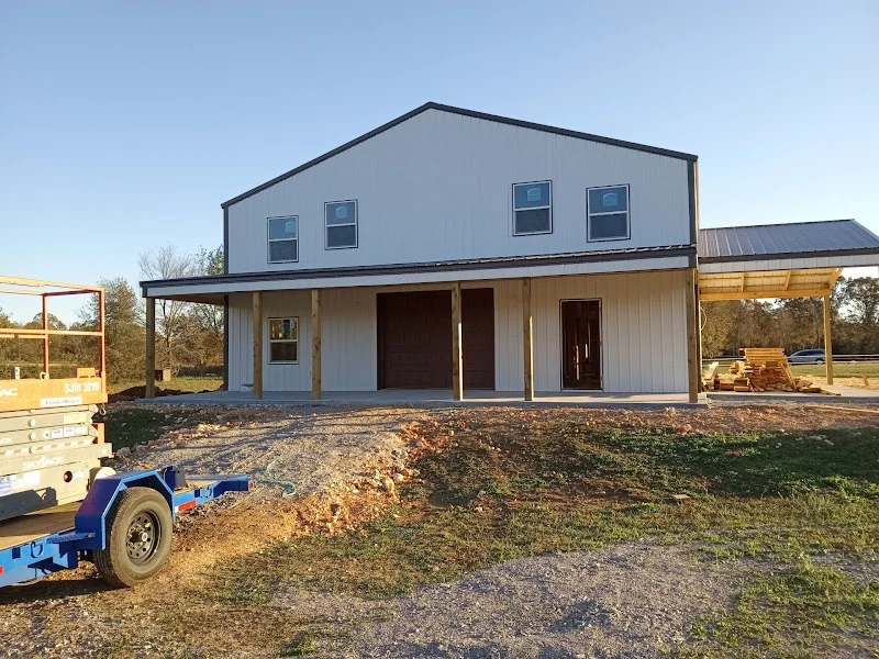 Elite Garage Door Services of Northwest ArkansasA large two-story building with a covered porch and a dark brown garage door in Northwest Arkansas, with construction materials nearby, indicating ongoing garage door installation. A blue utility trailer is visible in the foreground.