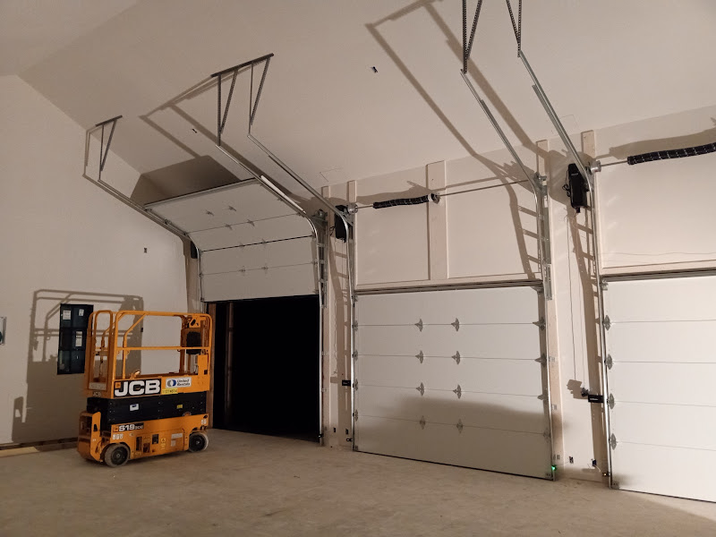 Elite Garage Door Services of Northwest ArkansasTwo white overhead garage doors are partially open inside a spacious garage, with an orange lift nearby. The scene illustrates a professional garage door installation, highlighting reliable service in Northwest Arkansas.