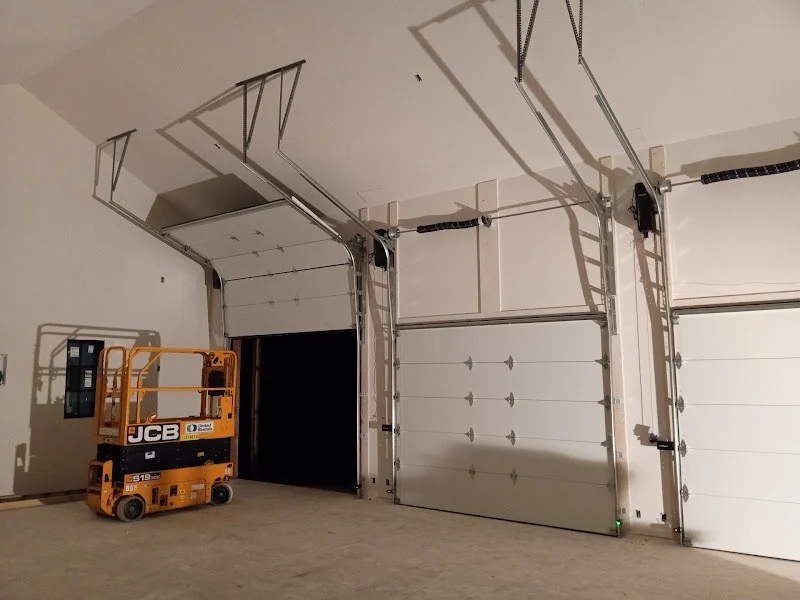 Elite Garage Door Services of Northwest ArkansasTwo white overhead garage doors are partially open inside a spacious garage, with an orange lift nearby. The scene illustrates a professional garage door installation, highlighting reliable service in Northwest Arkansas.