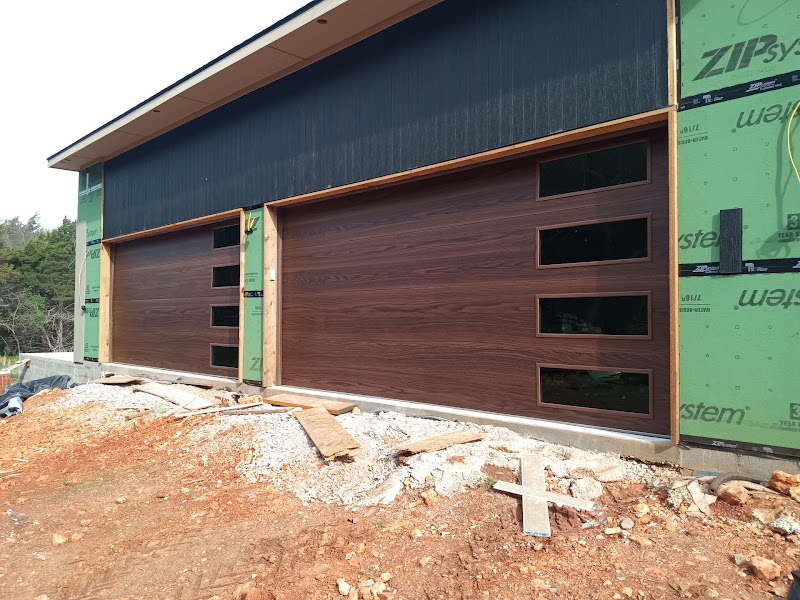 Elite Garage Door Services of Northwest ArkansasTwo newly installed residential garage doors with modern wood finish and windows are visible on a construction site in Northwest Arkansas, highlighting Elite Garage Door's professional and reliable garage door installation services in the area.