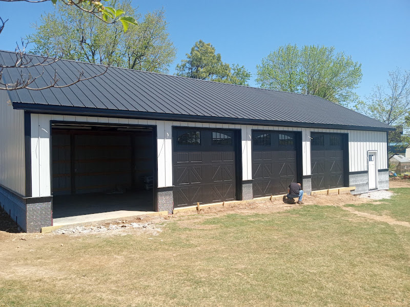 Elite Garage Door Services of Northwest ArkansasA professional technician from a local company in Northwest Arkansas is inspecting recently installed black residential garage doors on a sunny day, ensuring reliable operation and quality service for homeowners.