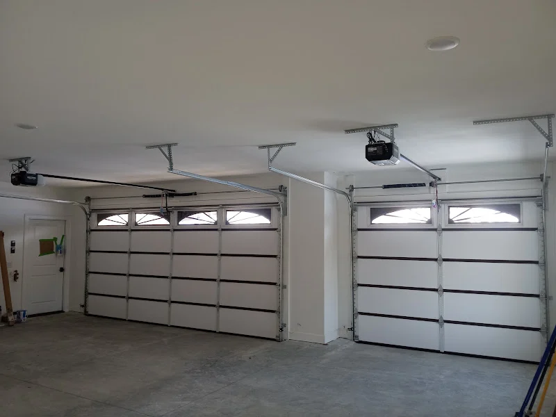 Elite Garage Door Services of Northwest ArkansasTwo white overhead garage doors with windows are inside a clean garage, equipped with modern garage door openers. This setup showcases residential garage doors, emphasizing reliable garage door service available in Northwest Arkansas.