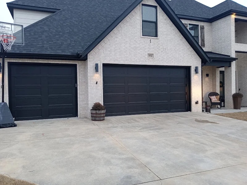 Elite Garage Door Services of Northwest ArkansasA modern house in Northwest Arkansas features two sleek black residential garage doors, highlighting the need for reliable garage door service and installation in the local area.