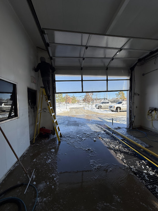 Elite Garage Door Services of Northwest ArkansasA professional technician in a hooded jacket repairs an overhead garage door in a snow-covered area, highlighting reliable garage door service in Northwest Arkansas.