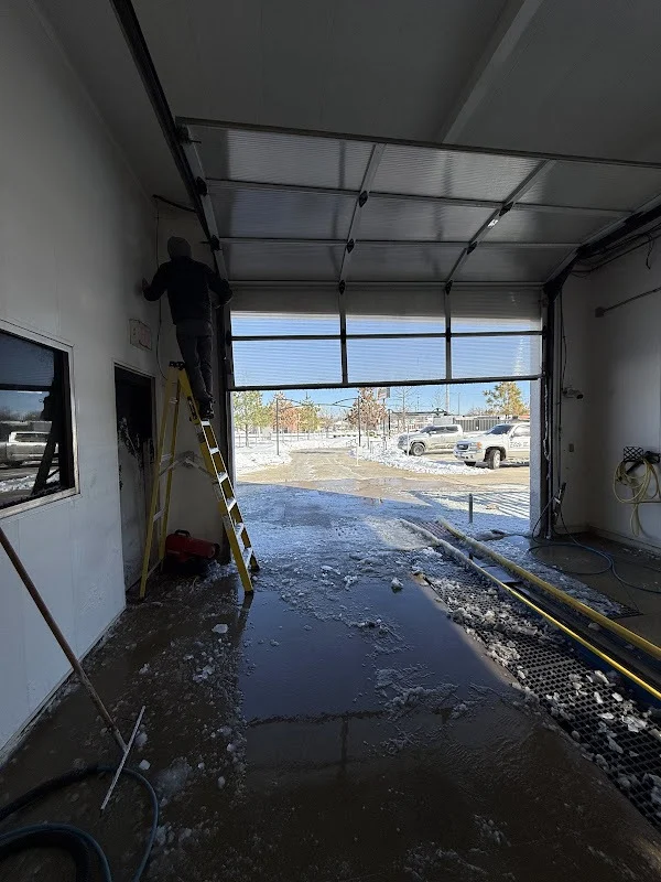 Elite Garage Door Services of Northwest ArkansasA professional technician in a hooded jacket repairs an overhead garage door in a snow-covered area, highlighting reliable garage door service in Northwest Arkansas.