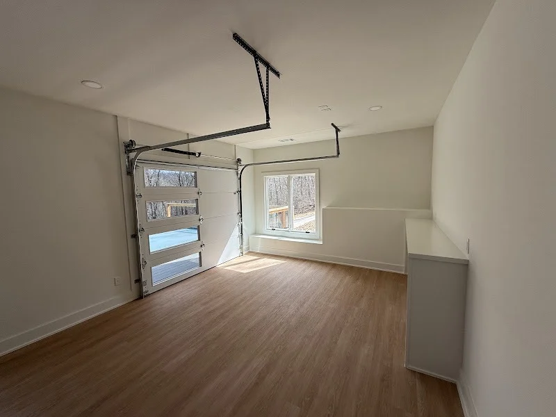 Elite Garage Door Services of Northwest ArkansasA newly installed overhead garage door in a bright, empty garage with light wood flooring and a large window. This residential garage door installation highlights the professional and reliable garage door service available in Northwest Arkansas.