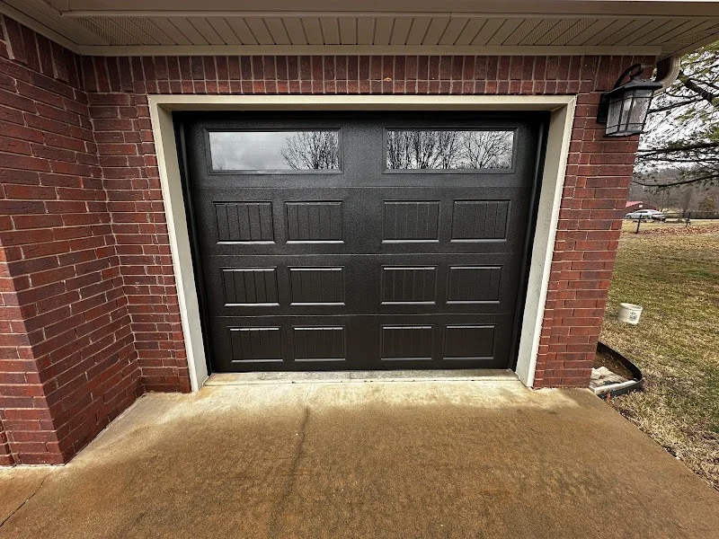 Elite Garage Door Services of Northwest ArkansasA newly installed black residential garage door with windows is set in a red brick exterior, showcasing a professional garage door service in Northwest Arkansas.