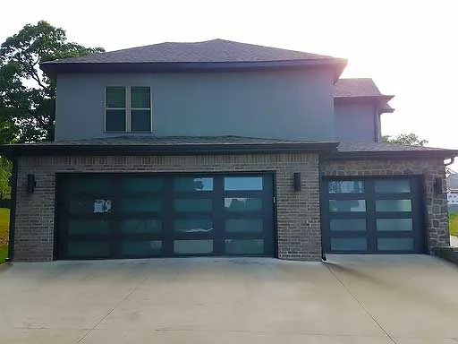 Elite Garage Door Services of Northwest Arkansas-A modern brick house in Northwest Arkansas features three sleek, black residential garage doors with frosted glass panels, showcasing a recent garage door installation in a local neighborhood.