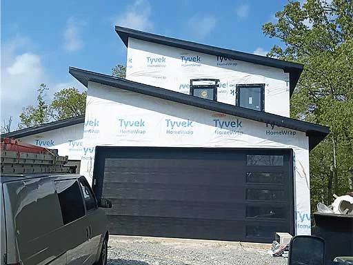 Elite Garage Door Services of Northwest Arkansas-A modern home in Northwest Arkansas with a newly installed black residential garage door. A van, possibly used for garage door installation, is parked in the driveway. The home exterior is wrapped in Tyvek, indicating ongoing construction.