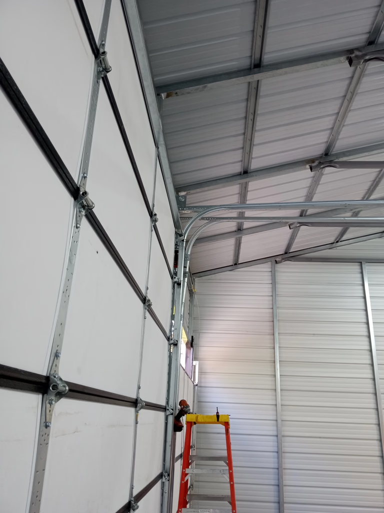 Elite Garage Door Services of Northwest ArkansasA professional technician stands on a red ladder performing garage door repair on overhead garage doors in a spacious, well-lit interior in Northwest Arkansas, emphasizing local, reliable service.