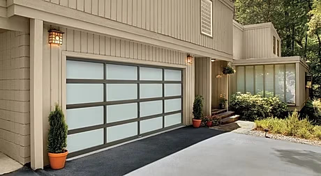 Elite Garage Door Services of Northwest ArkansasModern residential garage door with frosted glass panels on a beige house in Northwest Arkansas, surrounded by greenery and potted plants, showcasing reliable and professional garage door service available locally in NWA.