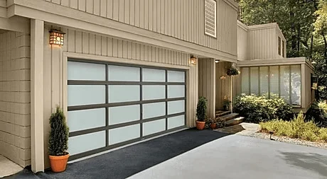 Elite Garage Door Services of Northwest ArkansasModern residential garage door with frosted glass panels on a beige house in Northwest Arkansas, surrounded by greenery and potted plants, showcasing reliable and professional garage door service available locally in NWA.