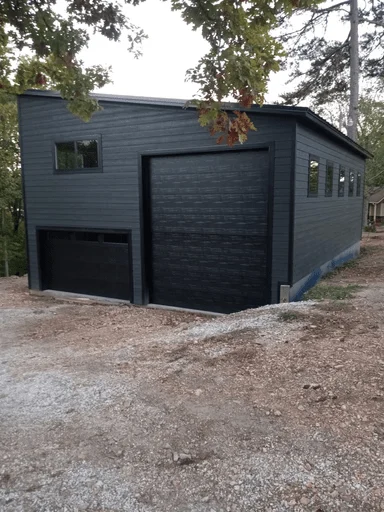 Elite Garage Door Services of Northwest ArkansasA modern, dark gray building with large overhead garage doors, situated in a wooded area, exemplifies potential garage door installation projects offered by professional services in Northwest Arkansas, including Fayetteville AR.