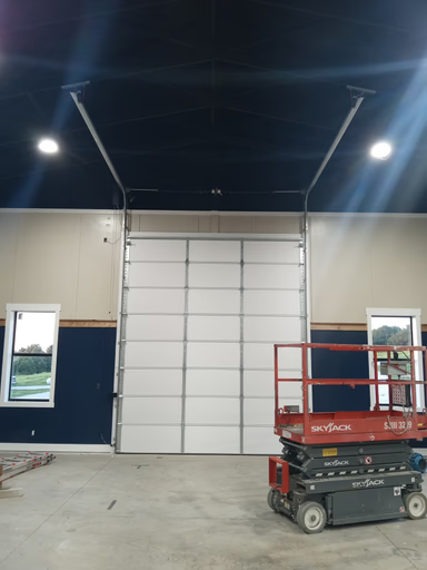 Elite Garage Door Services of Northwest ArkansasA large white overhead garage door is partially open inside a spacious industrial building, with a red scissor lift nearby. The scene reflects professional garage door installation in Northwest Arkansas, emphasizing reliable local service.