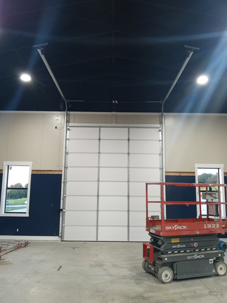 Elite Garage Door Services of Northwest ArkansasA professional technician in Northwest Arkansas uses a lift to install a large overhead garage door in a spacious interior, ensuring reliable garage door service.