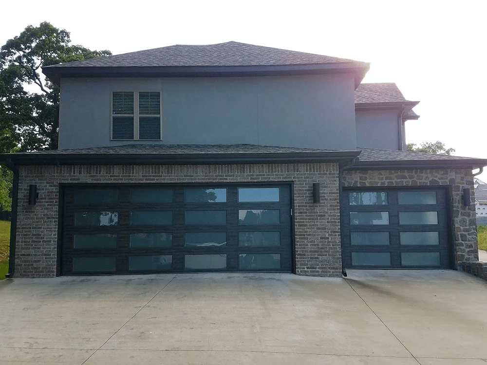 Elite Garage Door Services of Northwest ArkansasA modern home in Northwest Arkansas with two sleek, black residential garage doors offering reliable garage door service. The brick facade complements the contemporary style, reflecting professional installation and local expertise.