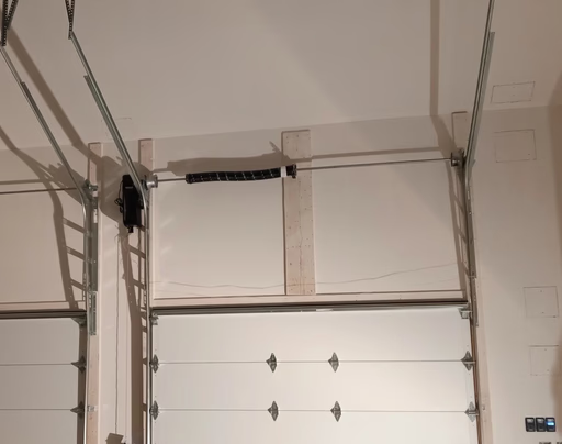 Elite Garage Door Services of Northwest ArkansasA professional technician from Elite Garage Door is inspecting garage door springs in a residential garage in Northwest Arkansas, ensuring reliable operation. The white overhead garage doors are part of a routine garage door service.