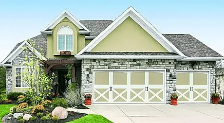 Elite Garage Door Services of Northwest ArkansasA beautiful stone and siding house in Northwest Arkansas features two white residential garage doors with crossbuck designs, showcasing a recent garage door installation. The well-maintained landscape enhances the home's curb appeal.