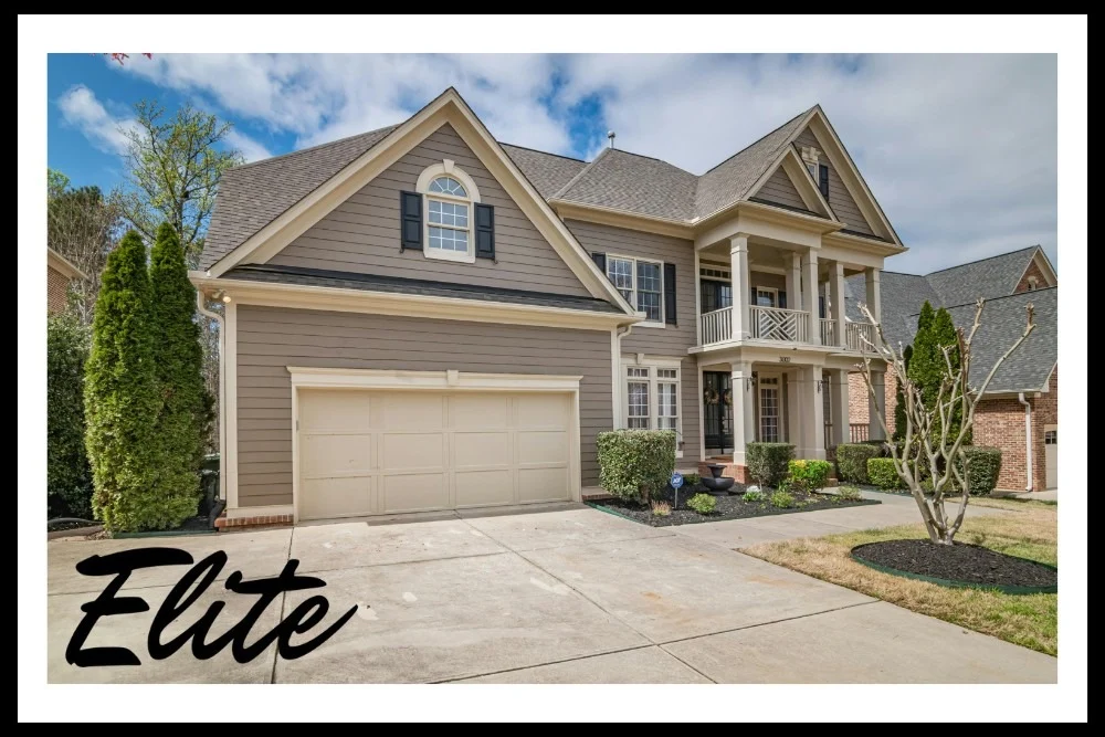 Why Regular Garage Door Tune-Ups Save You Money-2 Elite Garage Door Services of Northwest Arkansas-A beautiful beige house in Northwest Arkansas with a two-car residential garage door. The driveway is clean, and the landscaping is neatly maintained, showcasing professional garage door service. Elite branding is visible on the image.